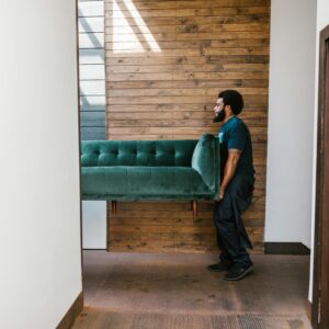 A mover carries a green sofa indoors, showcasing modern interior design and relocation services.